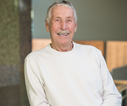 Man with grey hair posing for an indoor photograph, smiling.