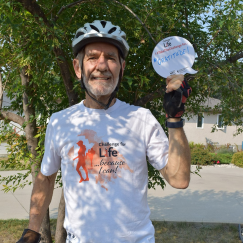 older man with grey hair and beard standing with bicycle and gratitude sign.