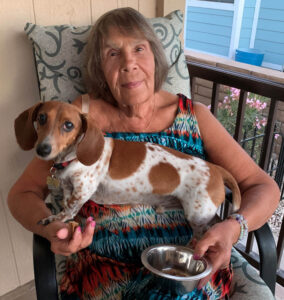 elderly lady sitting on a balcony with her small white and brown spotted dog in her lap. 