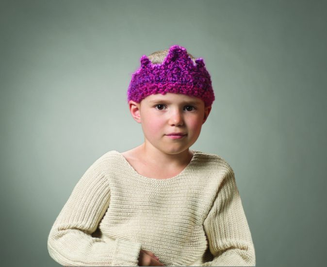 Little girl living through cancer treatment wearing a purple knitted crown.